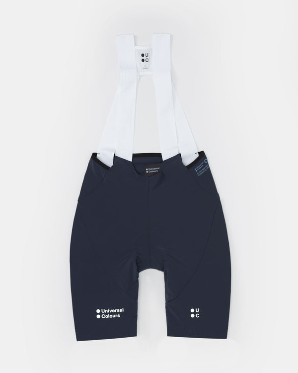 Flatlay of the Women's Chroma Bib Short in Navy Blue with white mesh bib straps and Universal Colours leg logos.