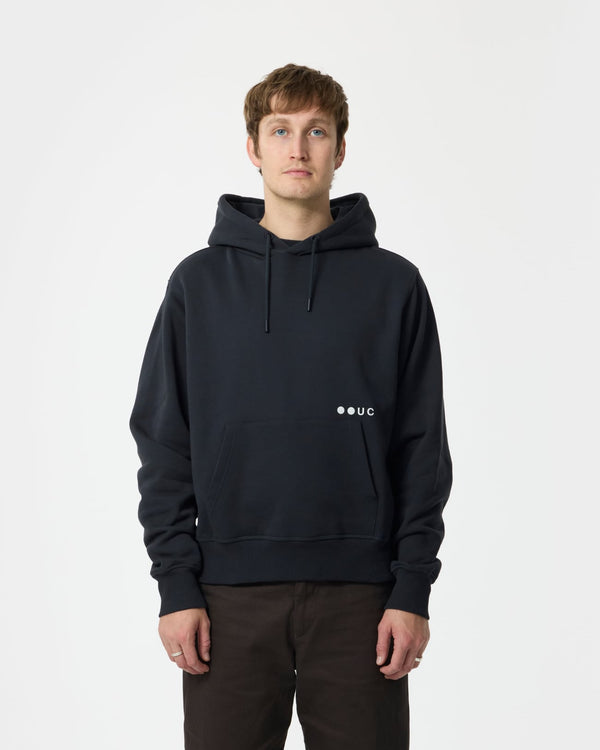 Male model wearing the Unisex Hoodie in Charcoal Black, front view, paired with brown trousers.
