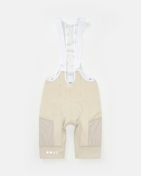 Flatlay of the Men's Mono Cargo Bib Shorts in Off White: tonal cargo side panels, white bib straps and UC back-yoke roundel.