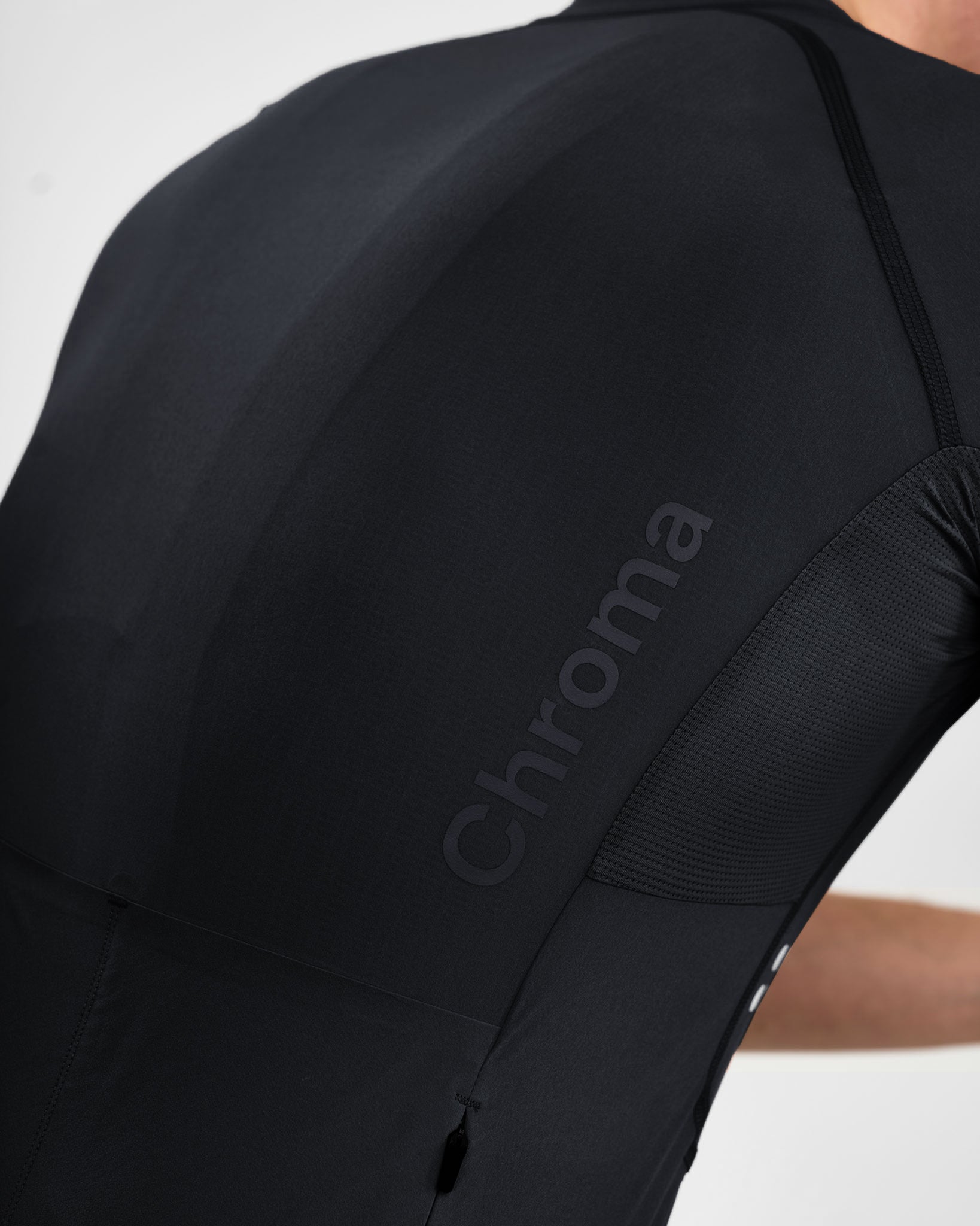 Back close-up: large tonal Chroma wordmark across the shoulder blade with mesh underarm panel on the Black jersey.