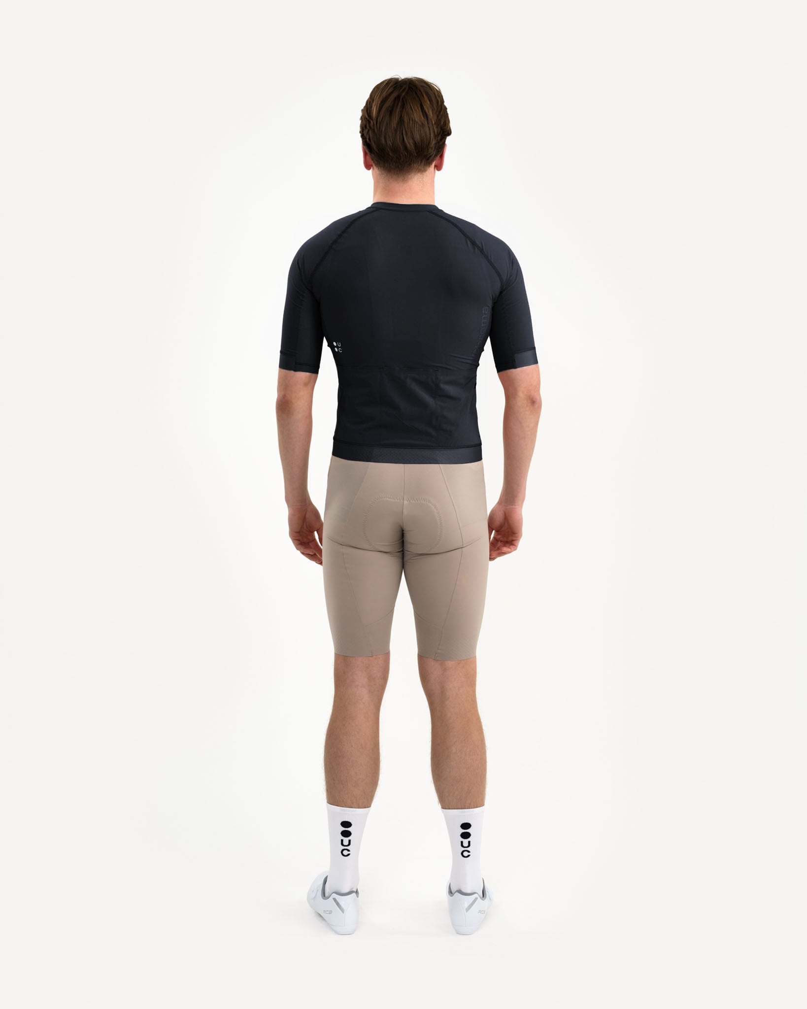 Full back view: model in the Men's Chroma Jersey in Black, white UC back logo, three rear pockets and gripper hem.