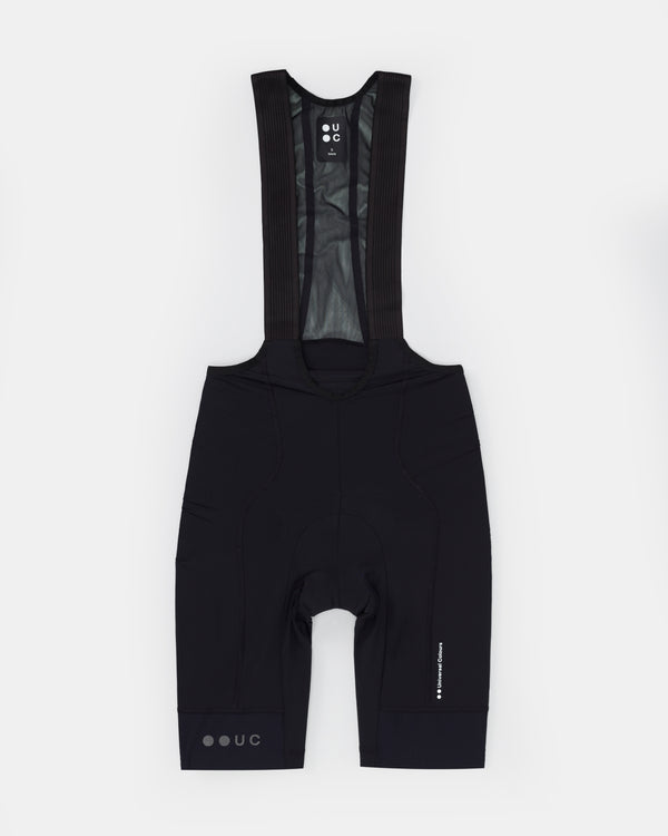 Men's Mono Bib Short 2.0 in Black, front flatlay: ribbed mesh bib straps, wide hem band and reflective UC leg branding.