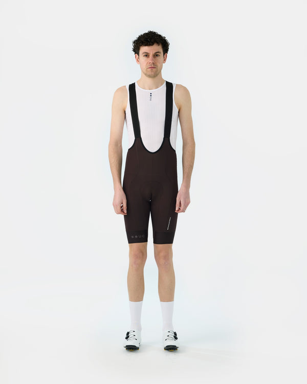 Model wearing the Men's Mono Bib Shorts 2.0 in Heavy Bark Brown, front view, paired with a white UC mesh base layer.