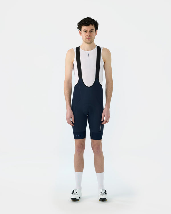 Model wearing the Men's Mono Bib Shorts 2.0 in Navy with a white mesh base layer, front view.