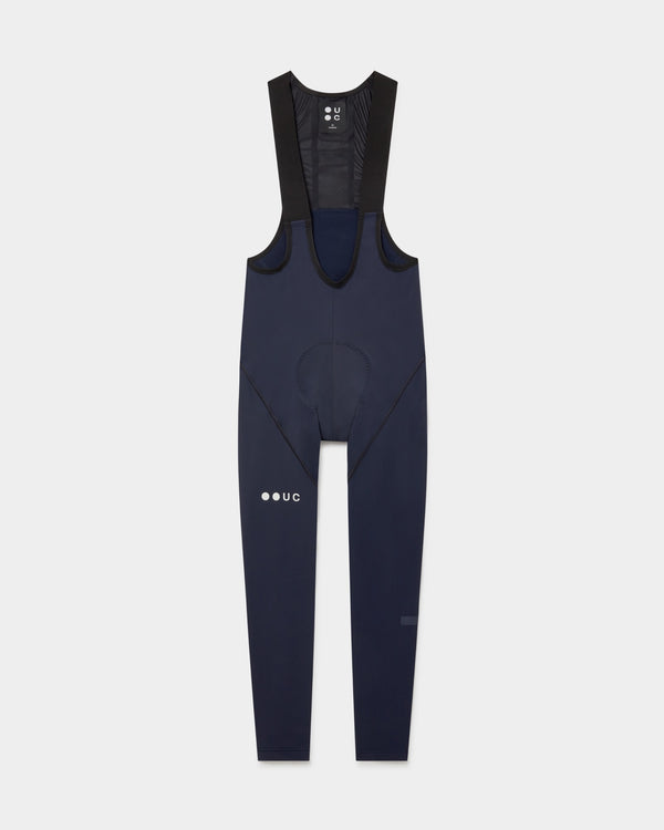 Flatlay of the Men's Mono Bib Tight in Navy Blue: black mesh bib straps, contoured chamois and white UC thigh logo.
