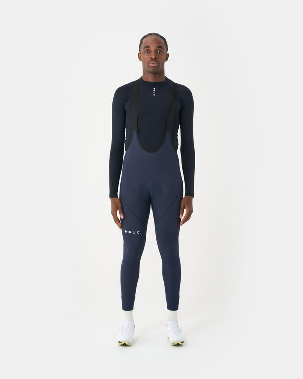 Front view: model wears the Men's Mono Bib Tight in Navy Blue over a black UC base layer with white socks and shoes.
