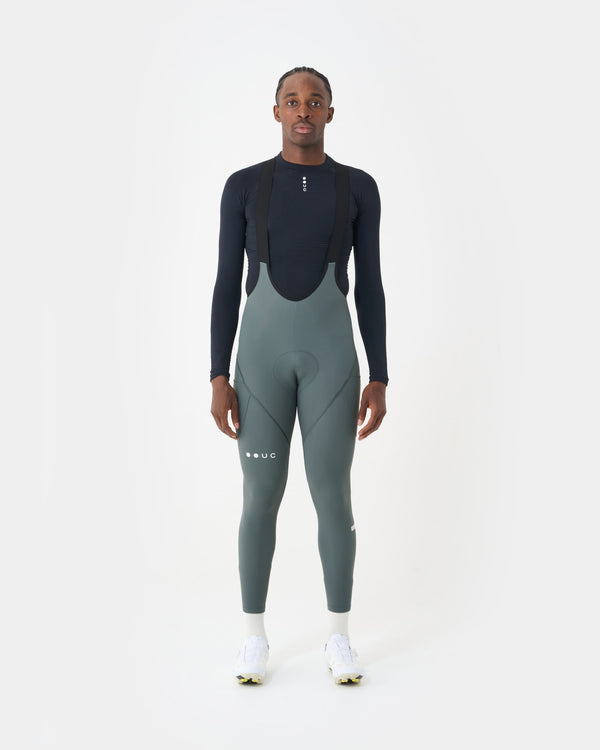 Model wearing the Men's Mono Cargo Bib Tight in Industrial Teal, front view, over a black UC long-sleeve base layer.