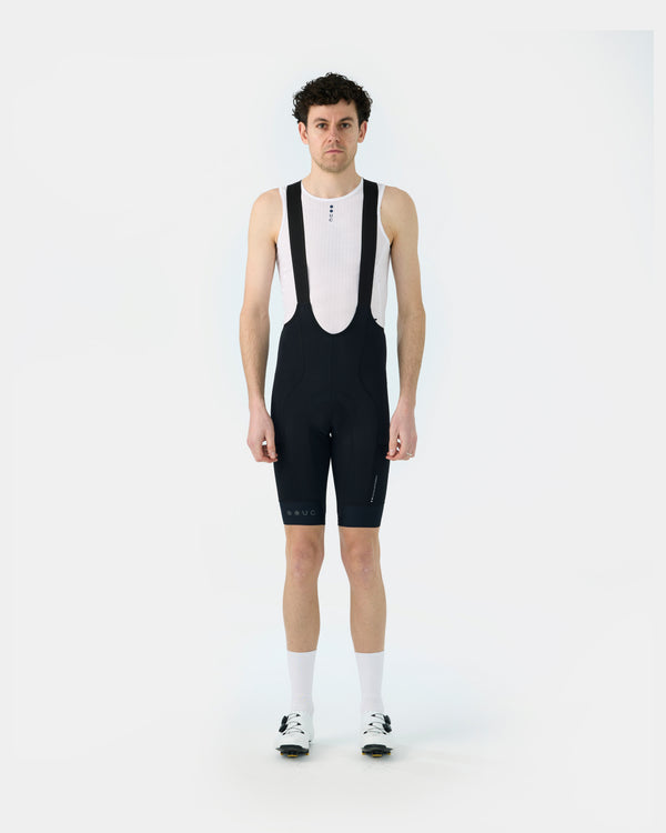 Model wearing the Men's Mono Cargo Bib Shorts in Black, front view, paired with a white UC base layer and cycling shoes.