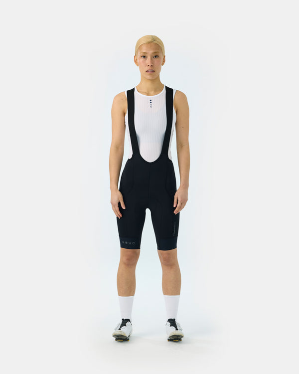 Model wearing the Women's Mono Cargo Bib Shorts in Black, front view, paired with a white UC base layer.