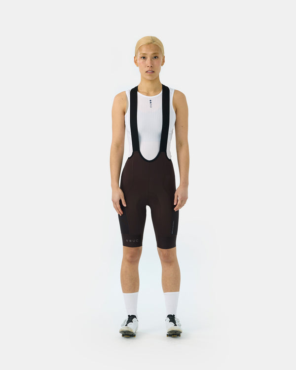 Model wearing the Women's Mono Cargo Bib Shorts in Heavy Bark Brown, front view, paired with a white UC mesh base layer.