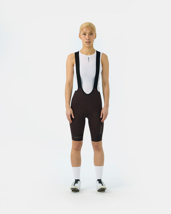 Model wearing the Women's Mono Bib Shorts 2.0 in Heavy Bark Brown with a white UC mesh base layer and white socks.