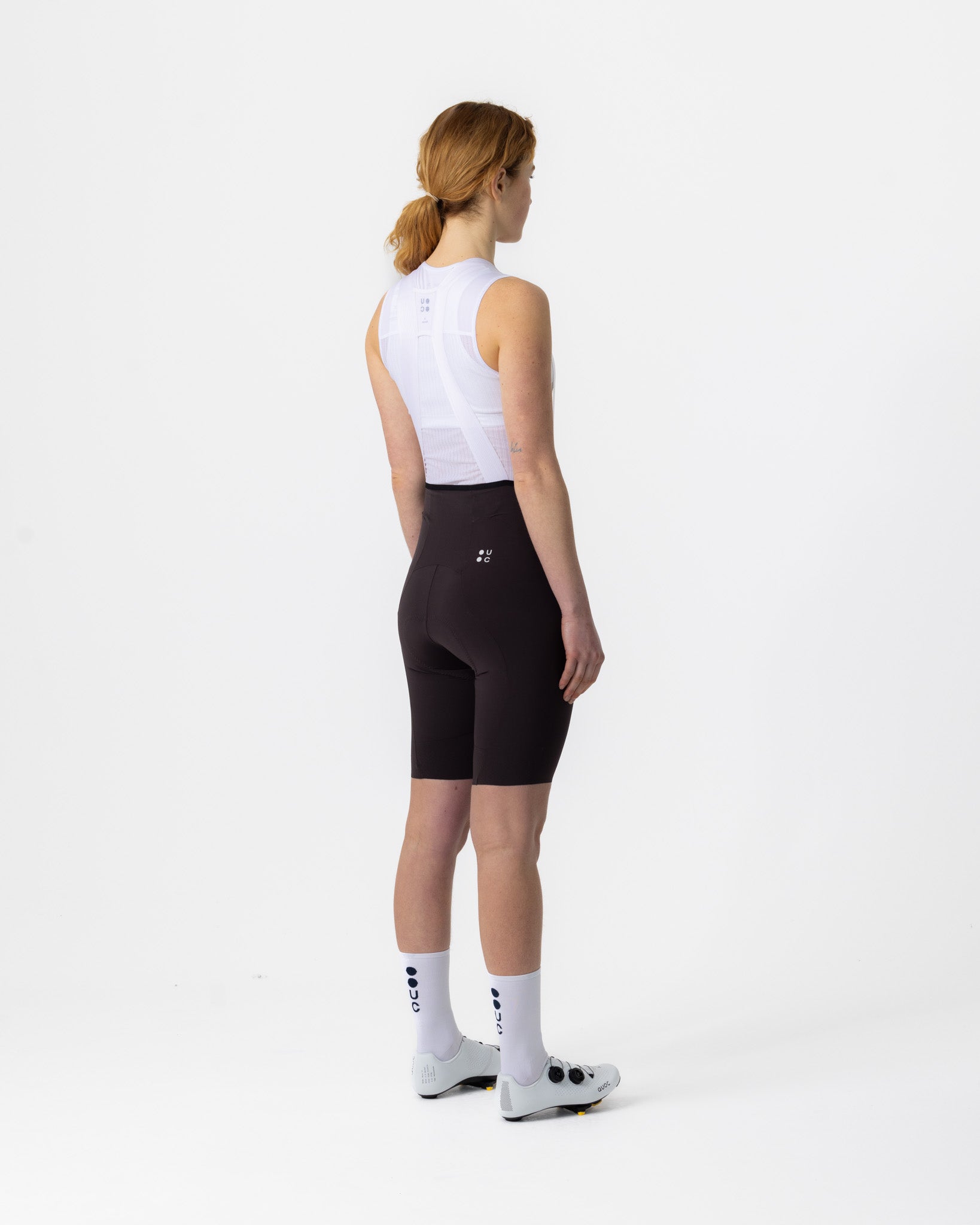 Three-quarter rear view: Women's Chroma Bib Shorts in Heavy Bark Brown with slim rear pocket and tonal UC back logo.