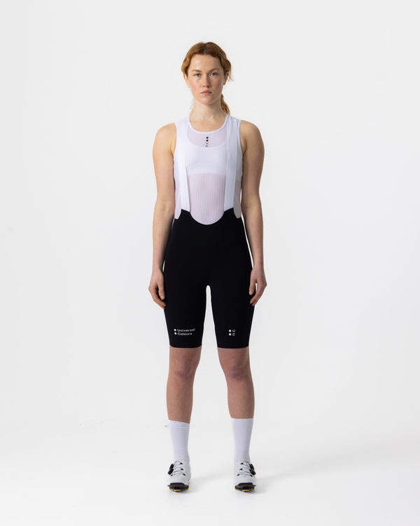 Model wearing the Chroma Women's Bib Short in Black, front view, paired with a white UC base layer and white socks.