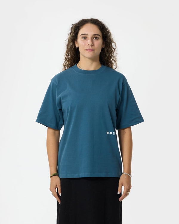 Model wearing the Unisex Short Sleeve Tee in Stone Blue, front view, relaxed boxy cut paired with a black skirt.