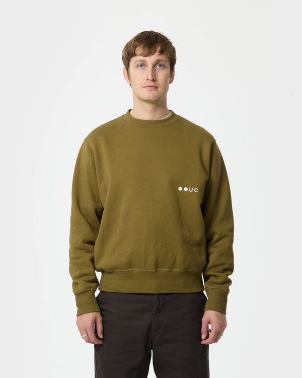 Model wearing the Unisex Sweatshirt in Wasabi Green, front view, styled with relaxed brown trousers.