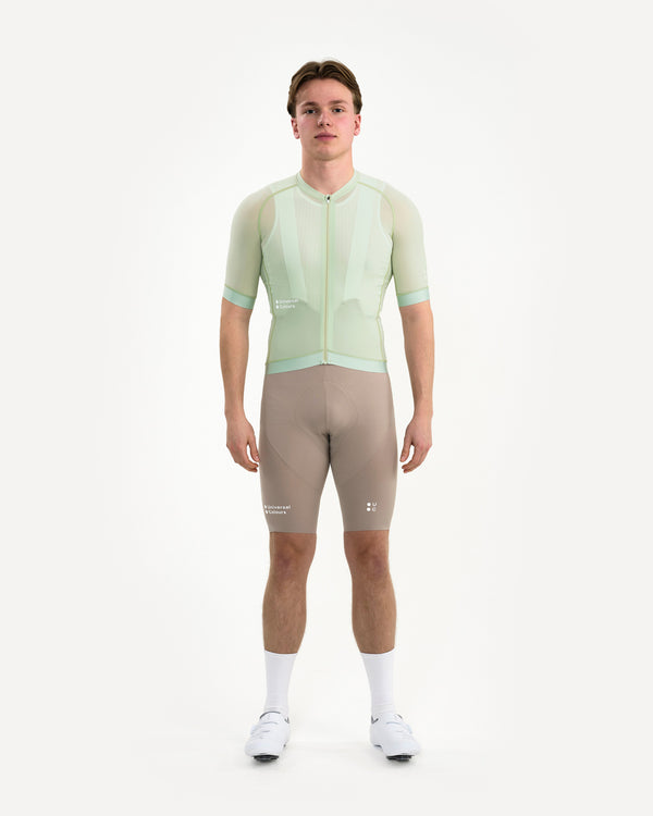Model wearing the Men's Chroma Light Jersey in Bower Green, paired with mosswood brown bib shorts and white socks.