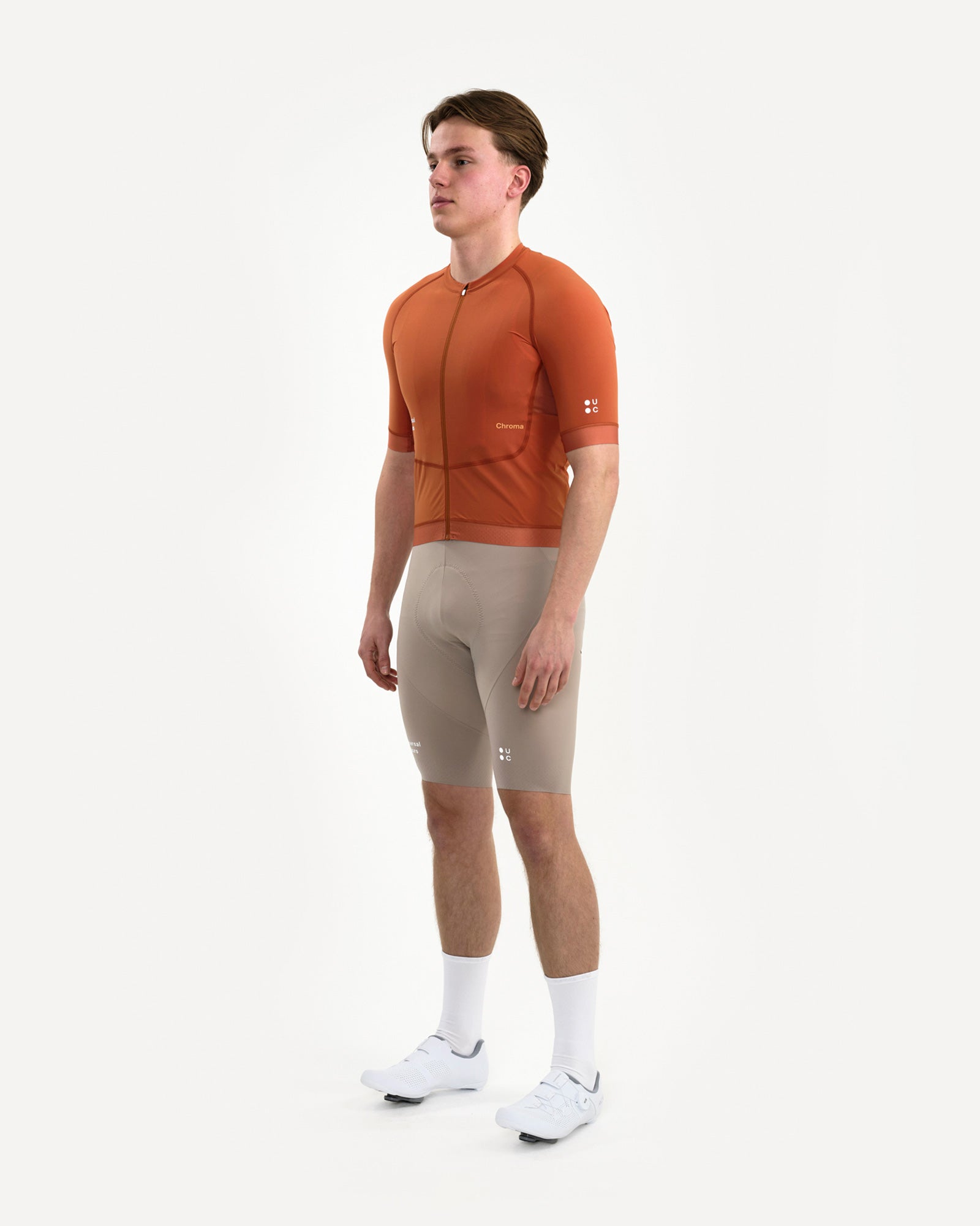 Three-quarter front: model in the Men's Chroma Short Sleeve Jersey in Cyprus Copper with stone bib shorts and UC socks.