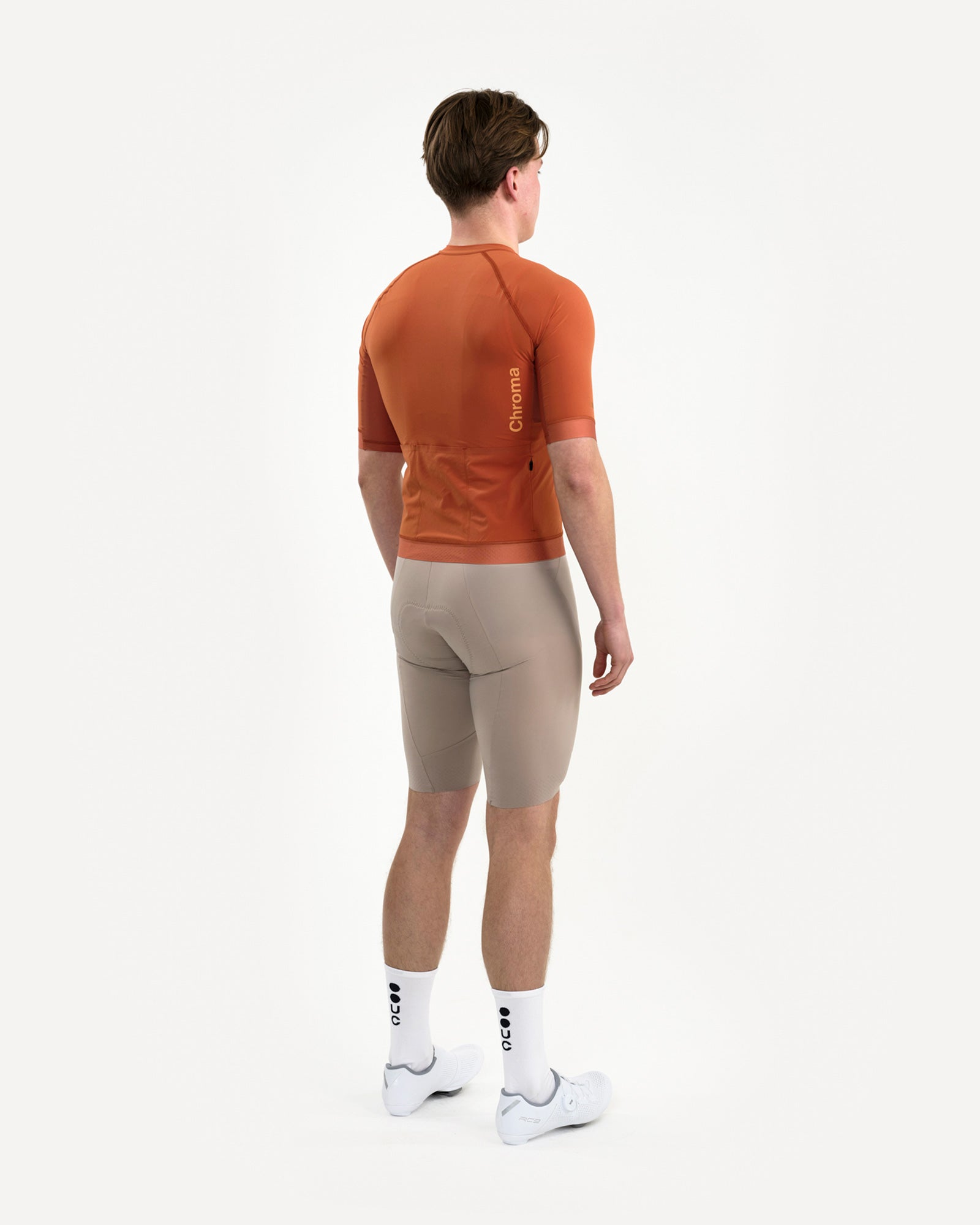 Rear three-quarter view of the Men's Chroma Short Sleeve Jersey in Cyprus Copper, worn with stone bib shorts.