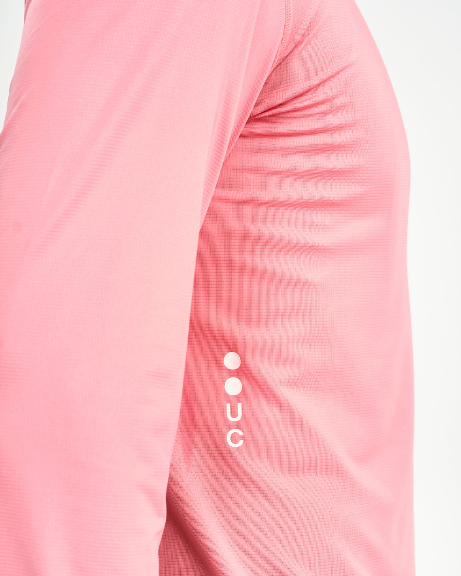 Upper-arm close-up of the Long Sleeve Tech Tee in Washed Pink, showing the tonal UC dot logo and waffle-knit tech fabric.