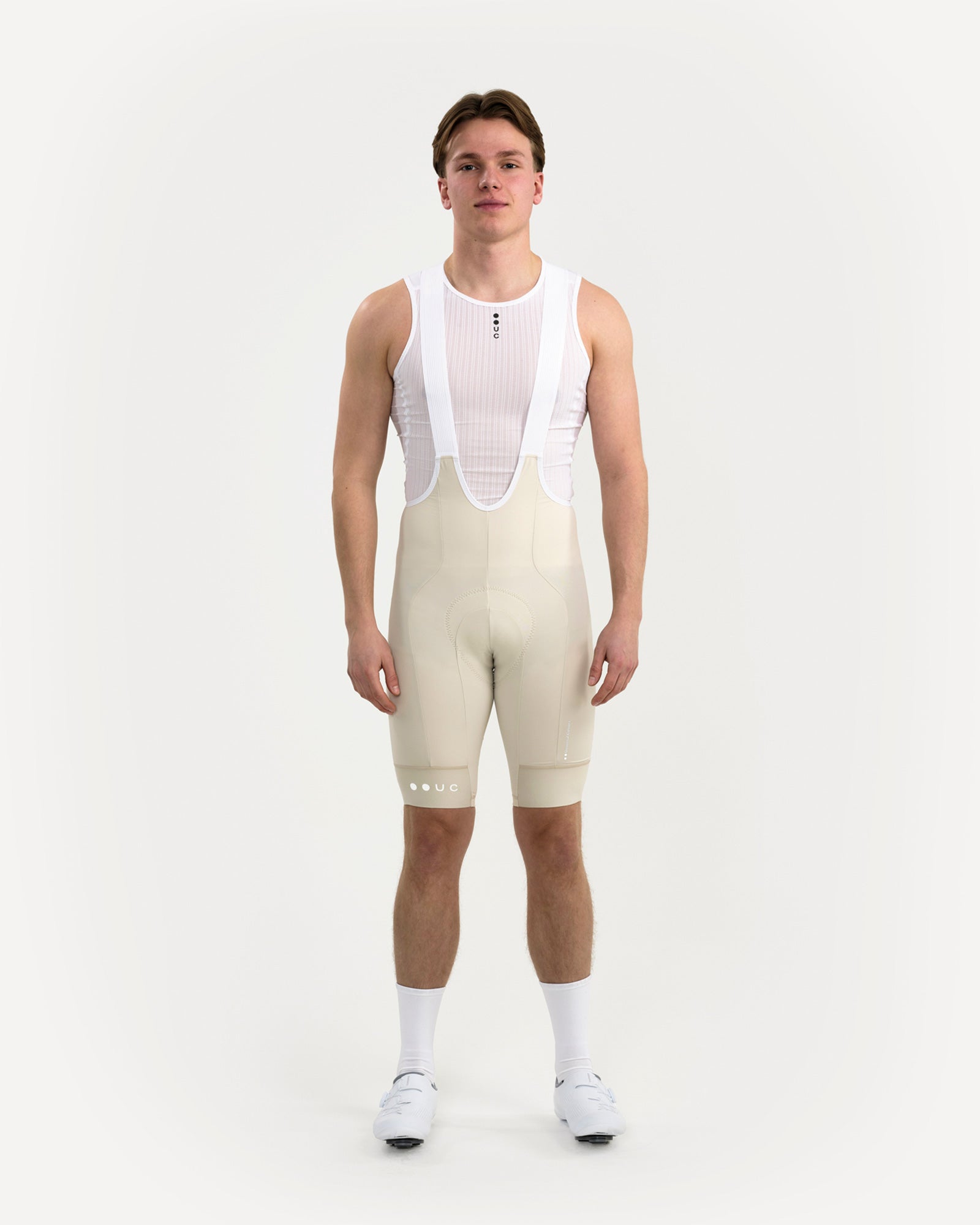 Front view: model wearing the Men's Mono Bib Shorts 2.0 in Off White with a white UC mesh base layer.