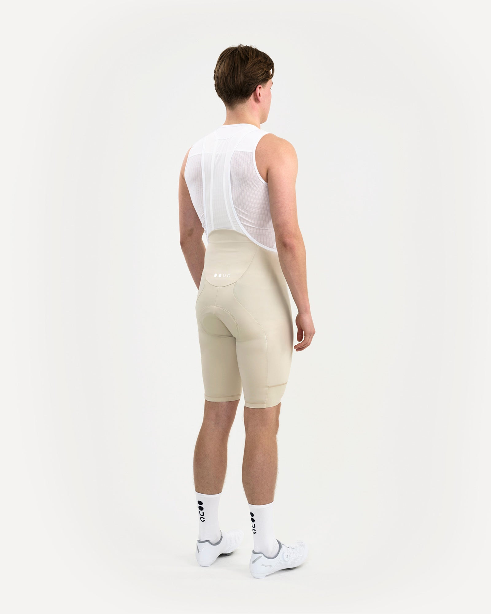 Back view of the Men's Mono Bib Shorts 2.0 in Off White, showing the heightened waist yoke and tonal UC logo.