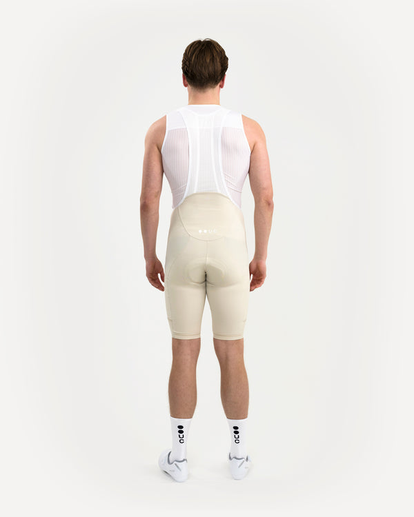 Model rear view: Men's Mono Bib Shorts 2.0 in Off White worn with white UC base layer, socks and shoes.
