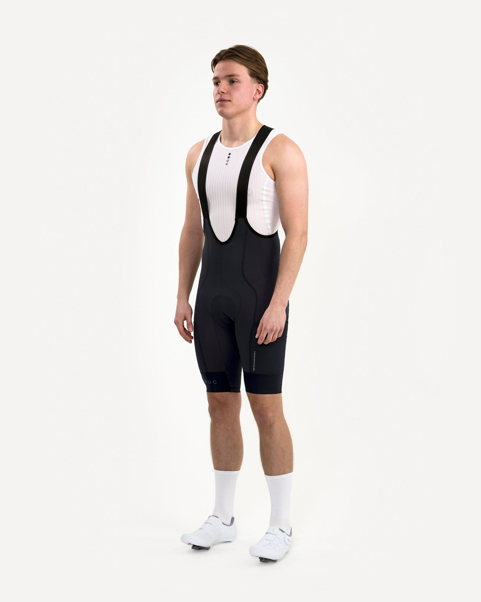 Three-quarter front: model in Men's Mono Cargo Bib Shorts Navy Blue with white UC base layer and tonal UC leg print.