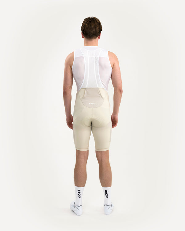 Model wearing the Men's Mono Cargo Bib Shorts in Off White, rear view, with a white mesh base layer and white UC socks.