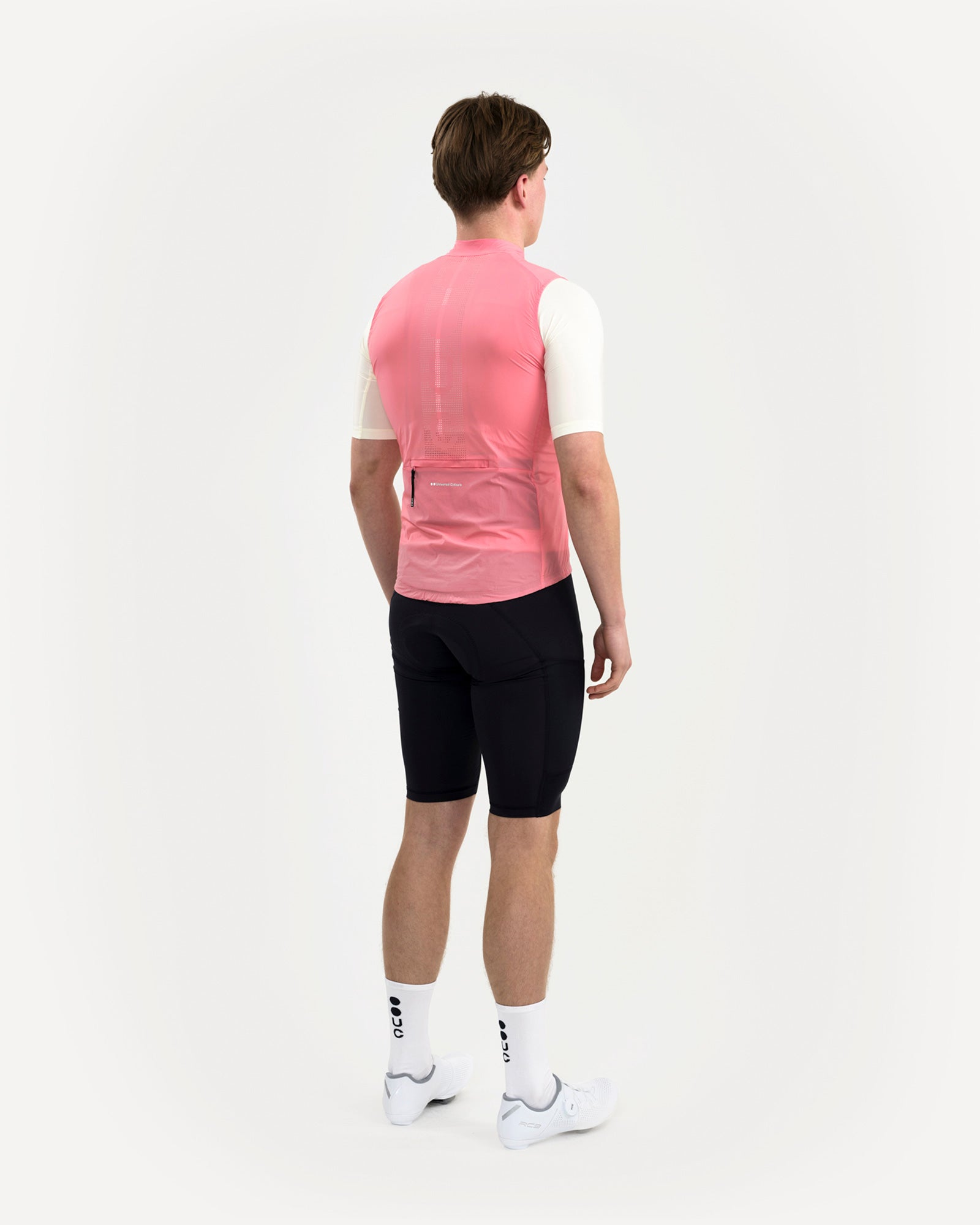 Model in the Men's Mono Gilet 2.0 in Washed Pink, three-quarter back view paired with black bib shorts.