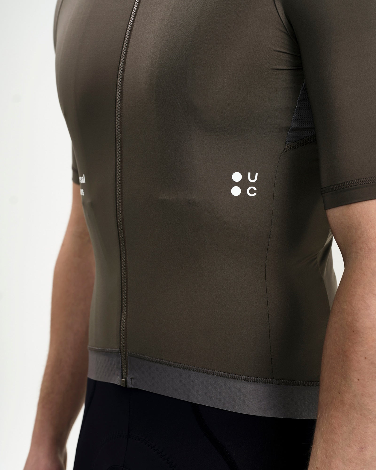 Close-up of the tonal UC dot logo on the Soft Grey Men's Mono Jersey, with silicone gripper hem and side mesh panel.