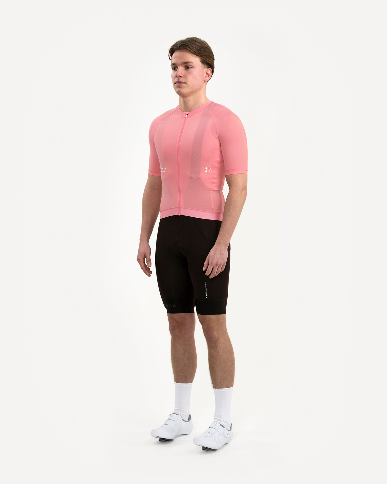 Three-quarter front view of the Men's Mono Short Sleeve Jersey in Pink, styled with black UC bib shorts and white UC socks.