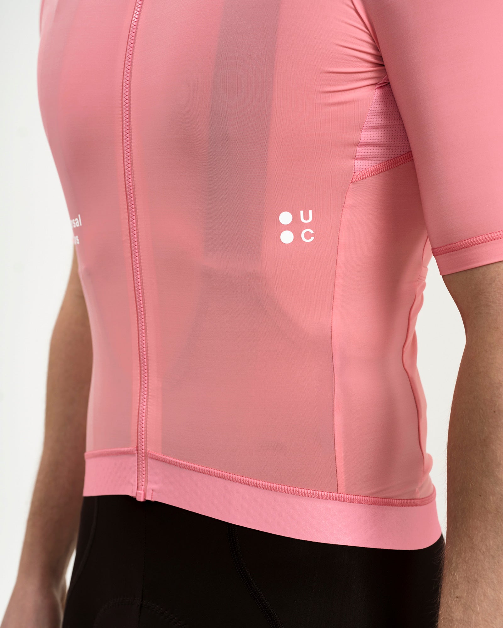 Side close-up of the Men's Mono Short Sleeve Jersey in Pink: white UC chest logo, mesh side panel and silicone gripper hem.