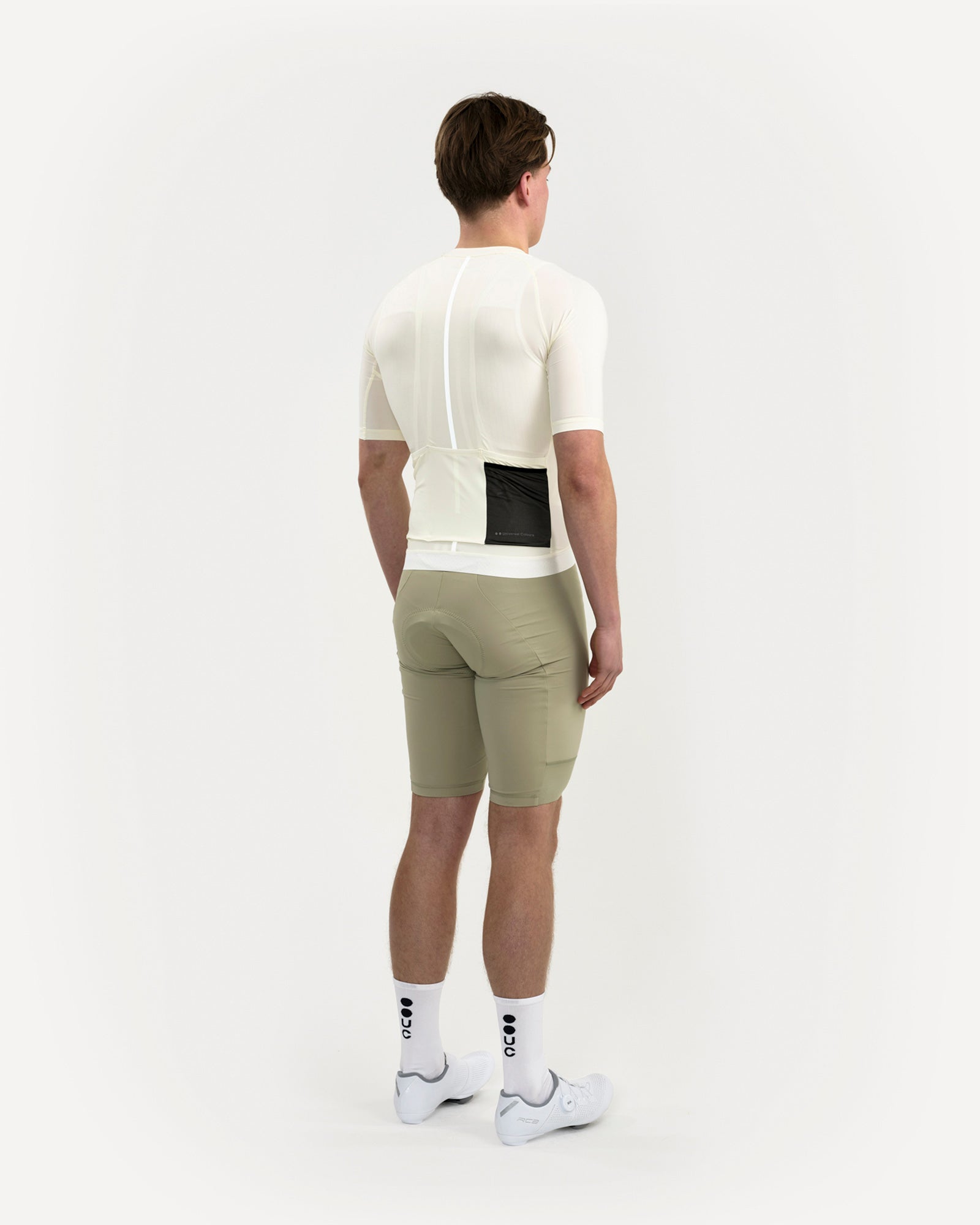Rear view: model in Men's Mono Short Sleeve Jersey in Tampered White, paired with sage green bib shorts and UC socks.