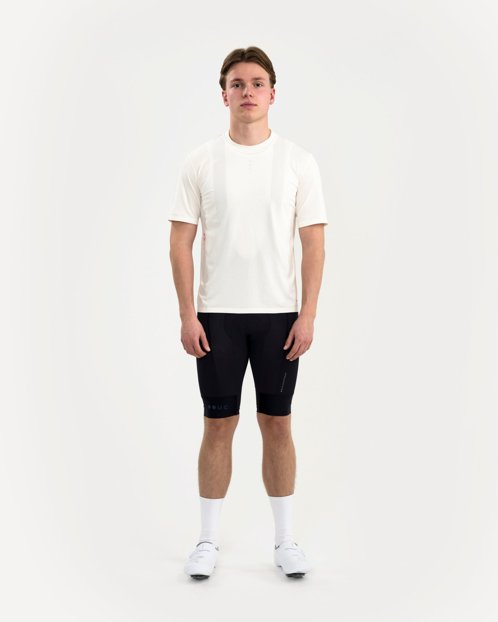 Front view: man wearing the Tech Tee in Off White with black cycling bib shorts and white road cycling shoes.