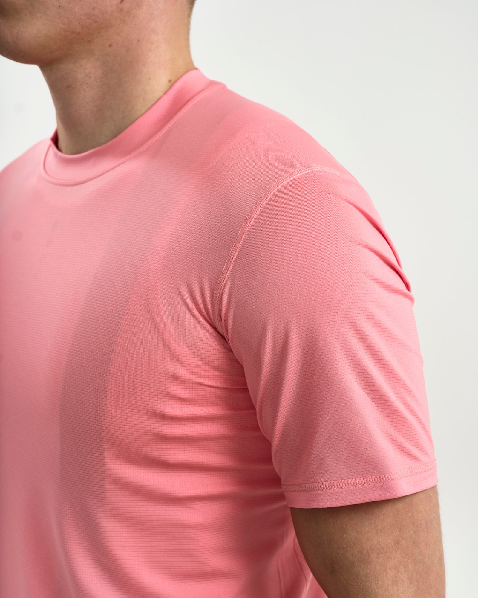 Close-up of the crew neck and raglan shoulder seam on the Tech Tee in Washed Pink, showing the ribbed mesh fabric.