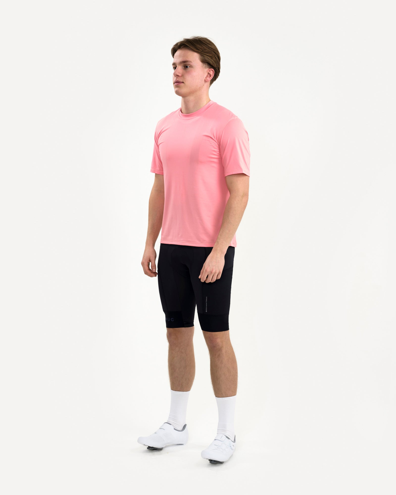 Three-quarter front view of a male model in the Tech Tee in Washed Pink and black UC cycling bib shorts.