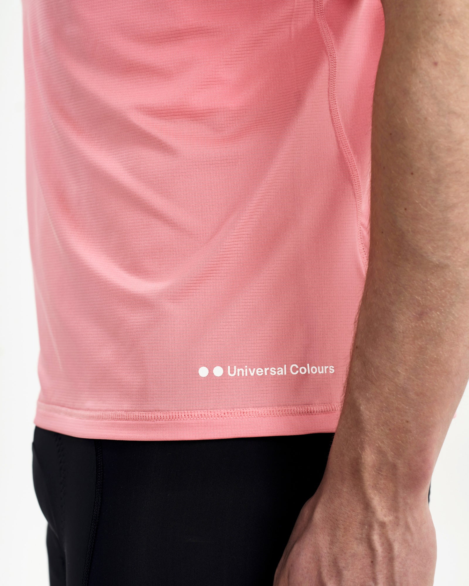 Front hem detail of the Tech Tee in Washed Pink: white Universal Colours wordmark and textured ribbed mesh fabric.