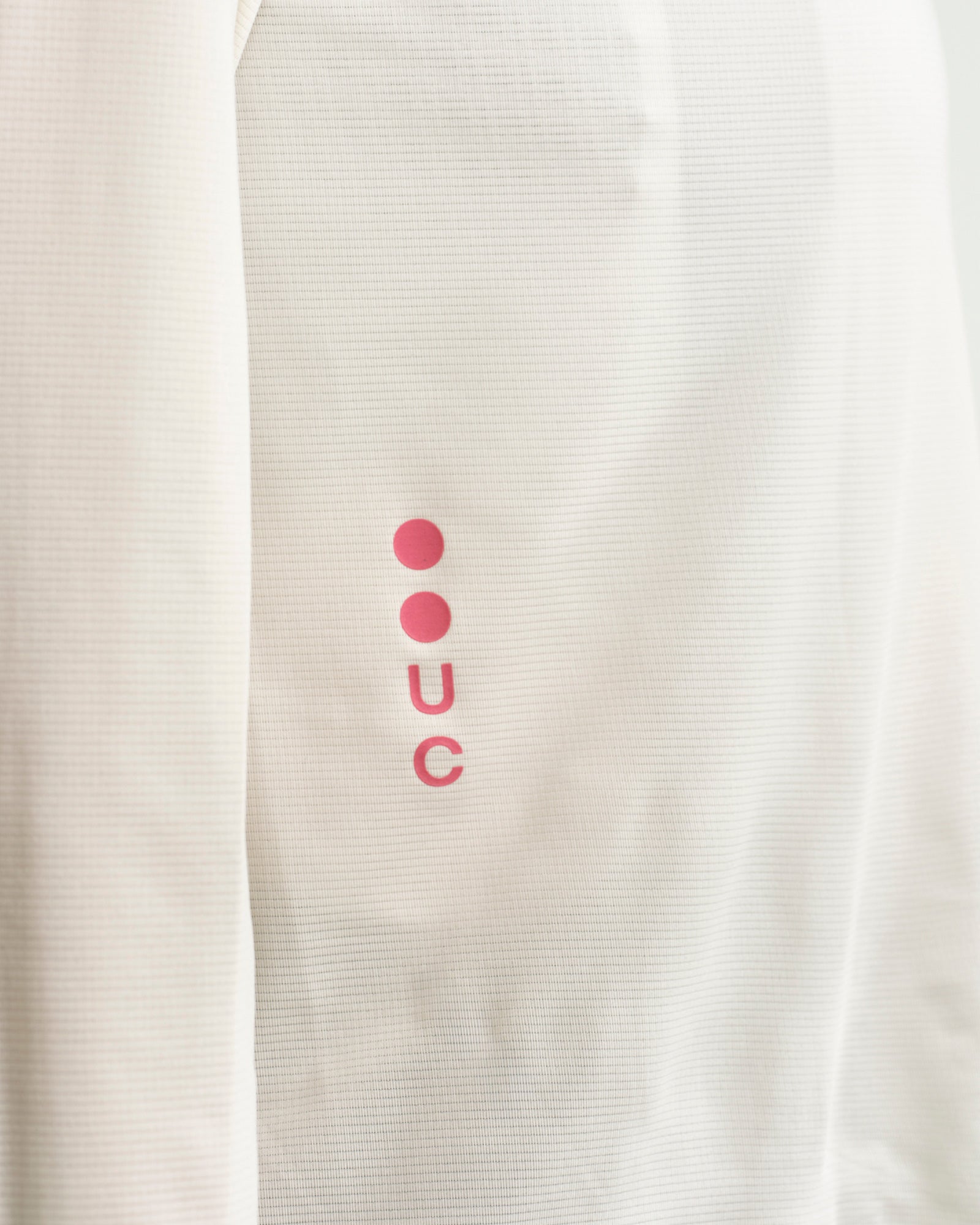 Close-up of the pink UC sleeve logo on the Long Sleeve Tech Tee in Off White, showing the lightweight ribbed fabric.