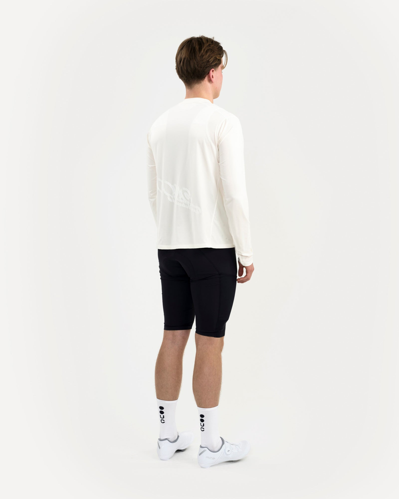 Three-quarter back view of the Long Sleeve Tech Tee in Off White on a male model, tonal UC graphic across the panel.
