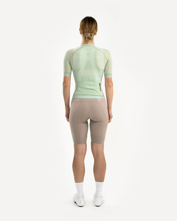 Back view: Women's Chroma Light Jersey in Bower Green, sheer mesh upper and rear zip pocket, worn with mushroom bib shorts.