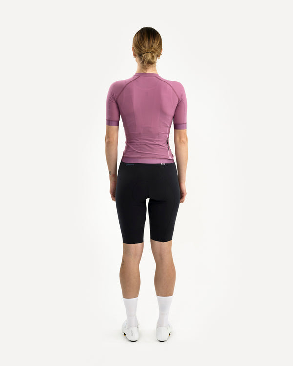 Back view: Women's Chroma Light Jersey in Dusty Lilac on model, side-rear zipped pocket visible, paired with black bibs.