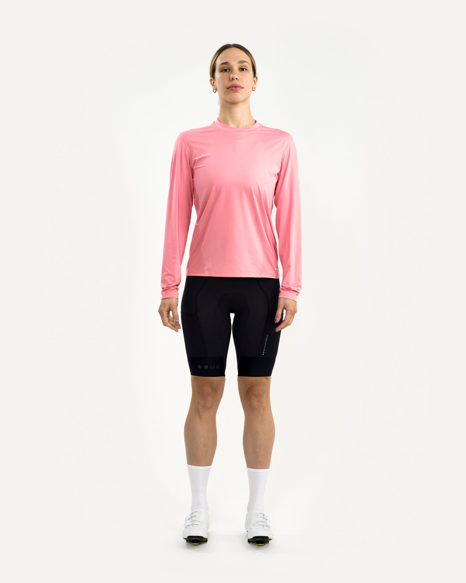 Women's front view of the Long Sleeve Tech Tee in Washed Pink, paired with black cycling bib shorts and white road shoes.