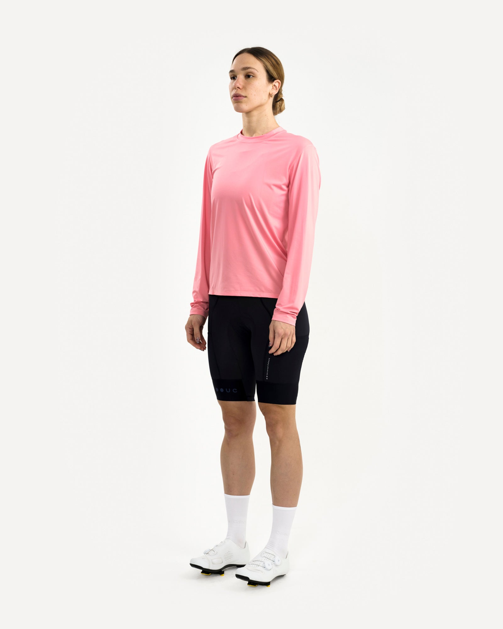 Women's front-three-quarter view of the Long Sleeve Tech Tee in Washed Pink, paired with black UC bib shorts and white shoes.