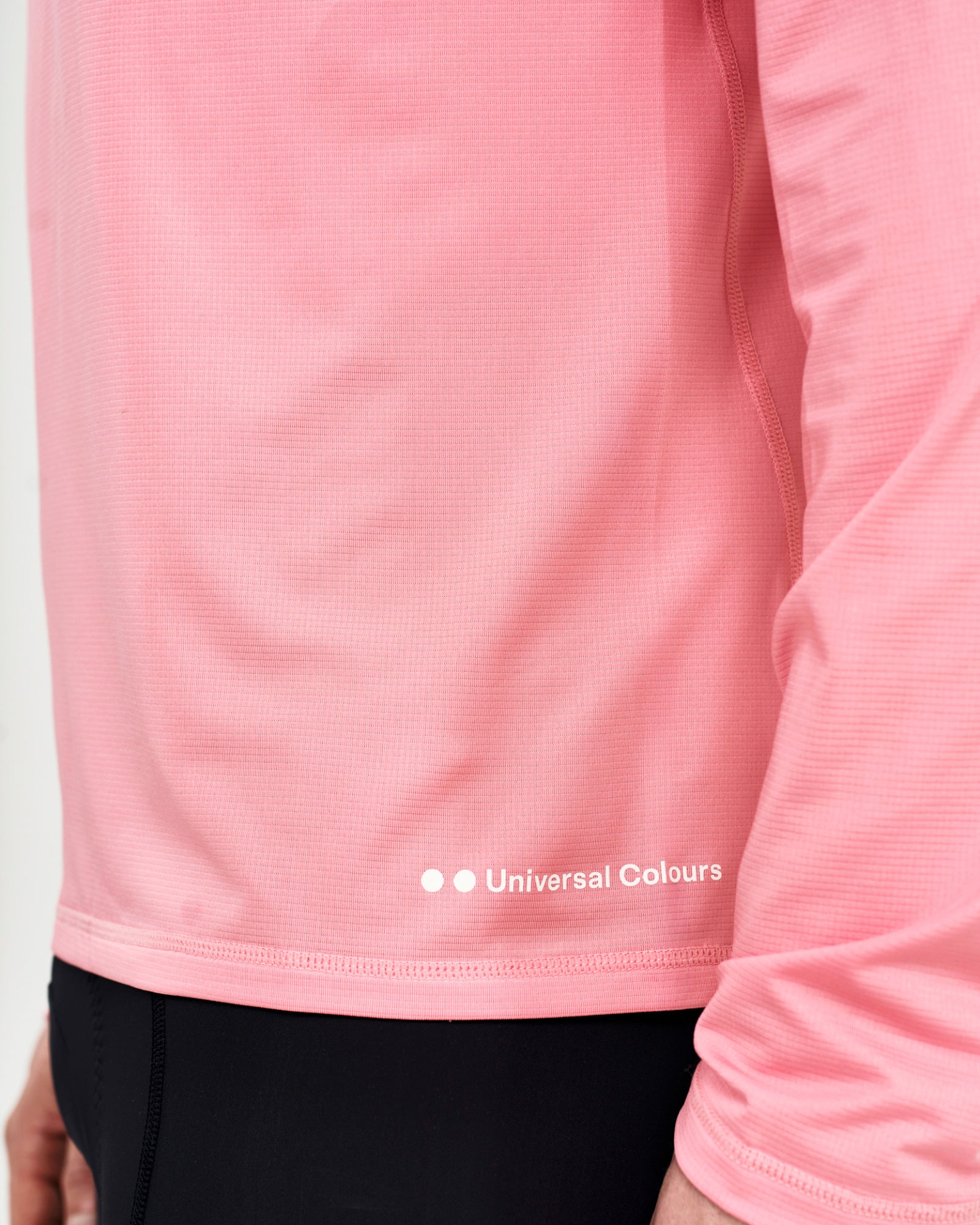 Hem detail of the Long Sleeve Tech Tee in Washed Pink: Universal Colours wordmark and waffle-knit tech-fabric texture.