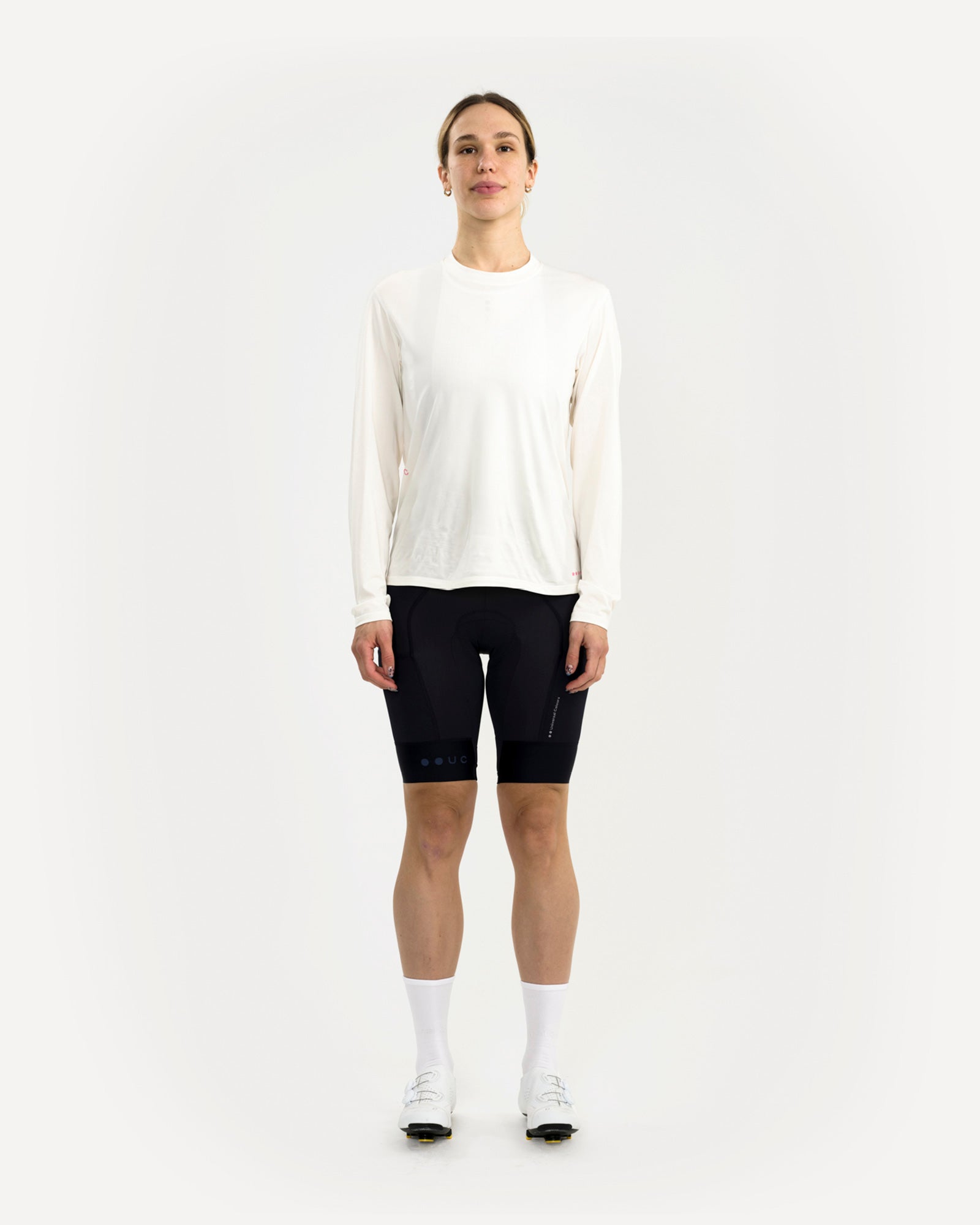 Female model wearing the Long Sleeve Tech Tee in Off White, front view, paired with UC black cycling bib shorts.