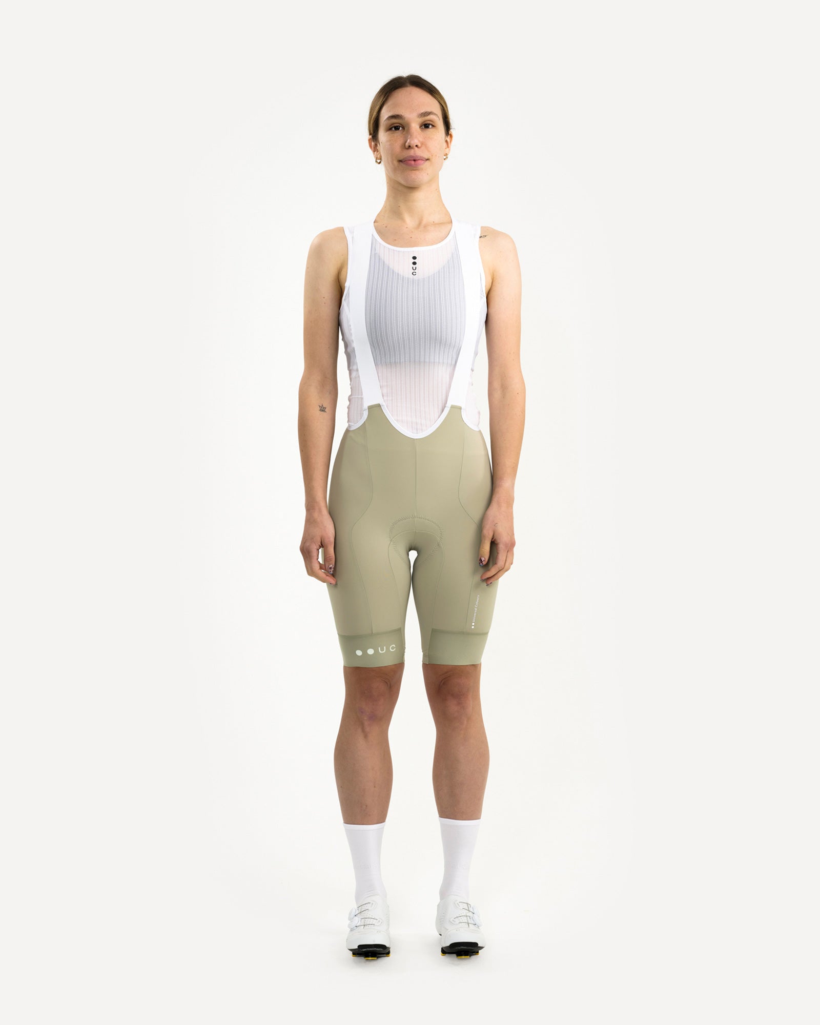 Front view: model in the Women's Mono Bib Shorts 2.0 in Green Tea, styled with white mesh base layer, socks and shoes.