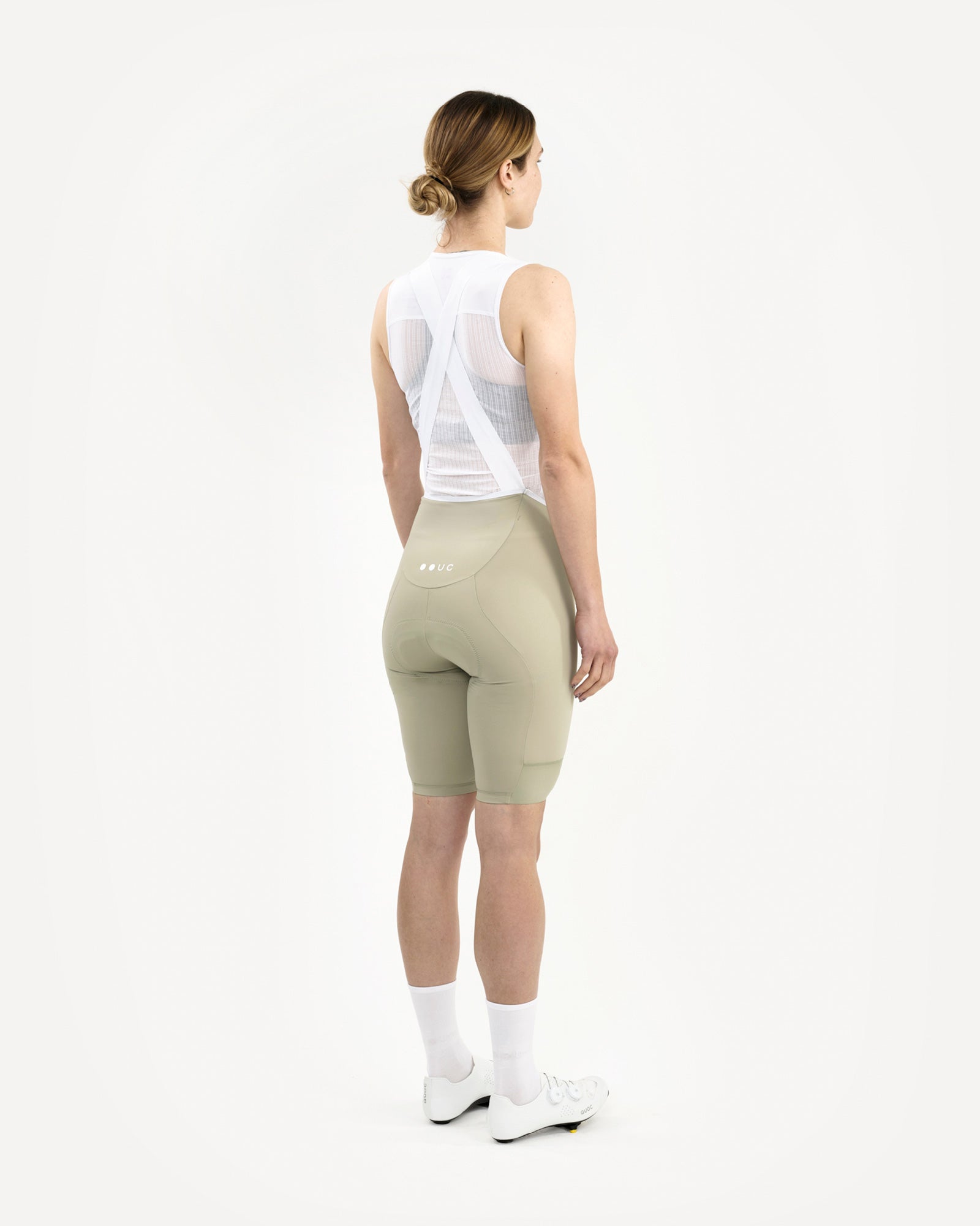 Three-quarter back view: Women's Mono Bib Shorts 2.0 in Green Tea, paired with a white mesh base layer and socks.