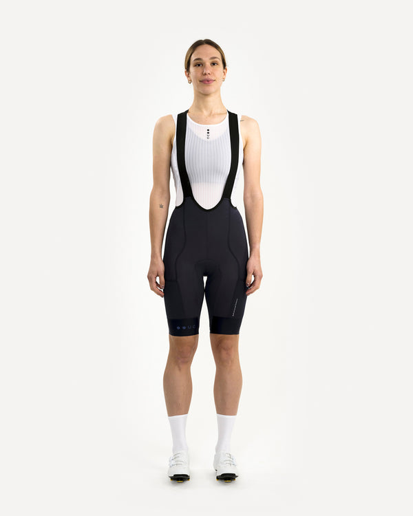 Model wearing the Women's Mono Cargo Bib Short in Navy Blue, front view, styled with white UC mesh base layer.