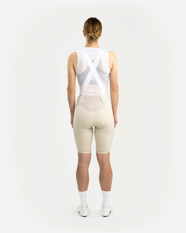 Model in the Women's Mono Cargo Bib Short, Off White, back view, paired with white sleeveless mesh base layer.