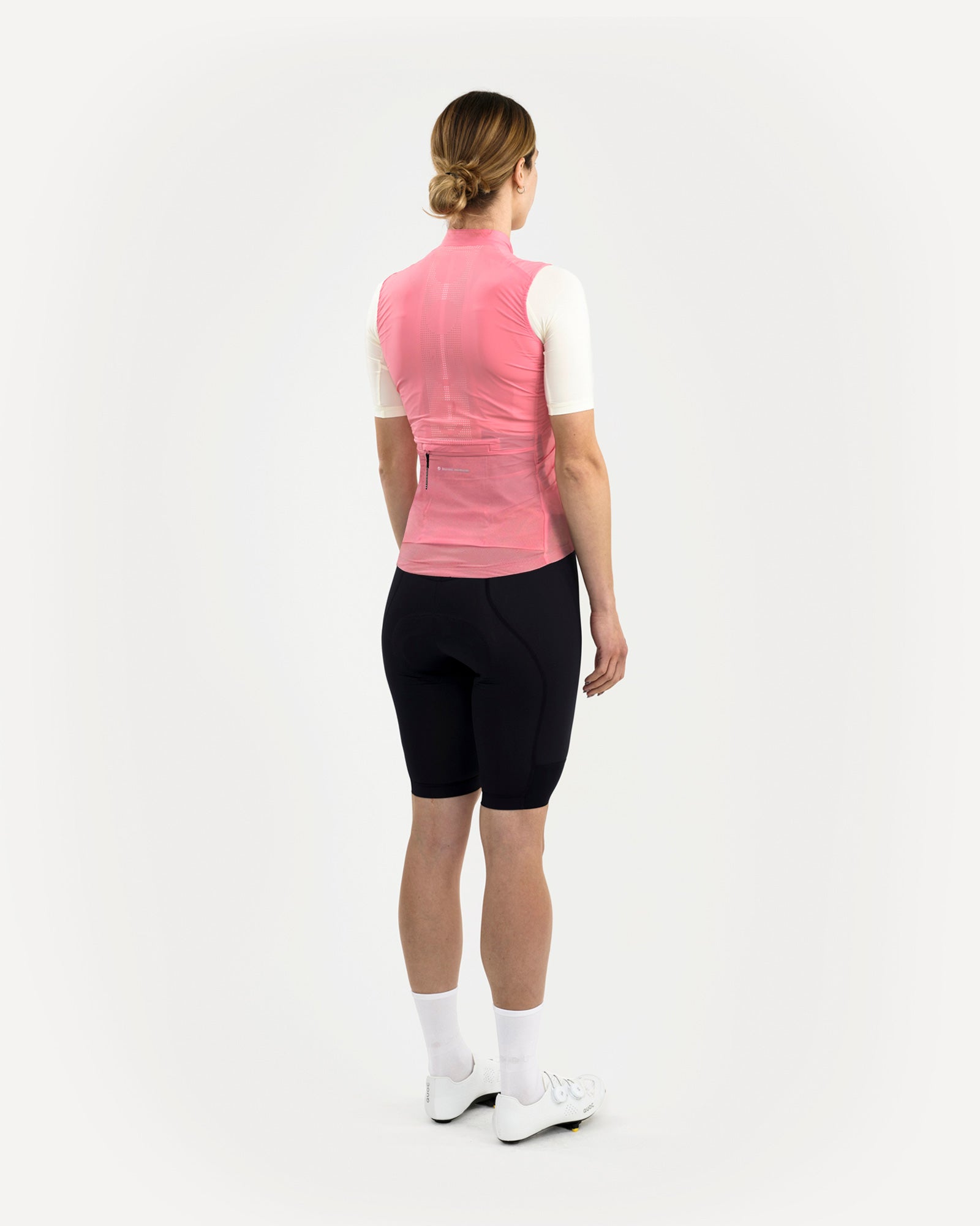 Three-quarter rear view: model wears the Women's Mono Gilet 2.0 in Washed Pink over a cream jersey with black bib shorts.